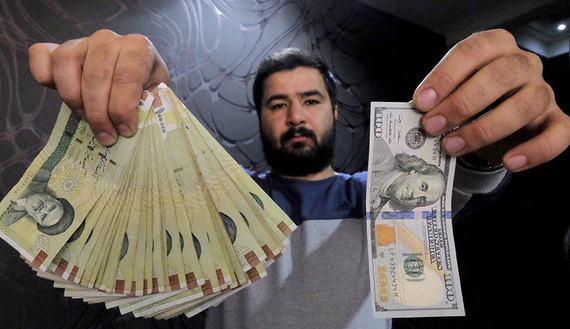 Money changer poses for the camera with U.S hundred dollar bill and the amount being given when converting it into Iranian rials, at a currency exchange shop in Tehran's business district, Iran